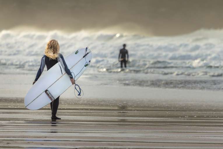 woman walking out to sea with surfboard