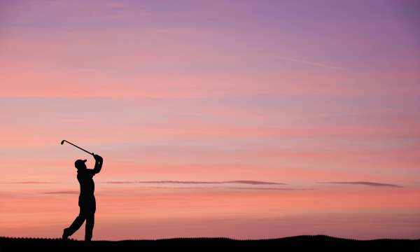 Golfer mid swing in sunset