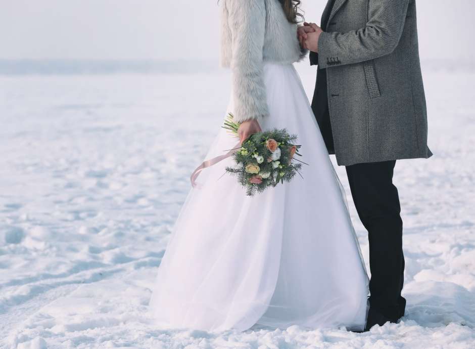 Bride and groom standing in snowy field at their winter wedding