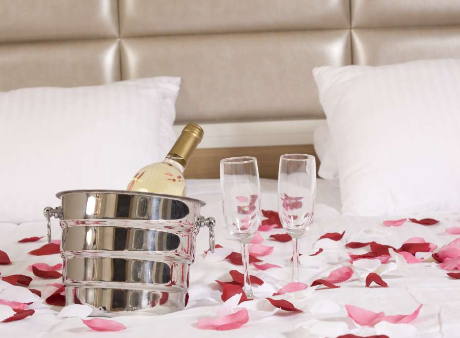 champagne and rose petals on bed