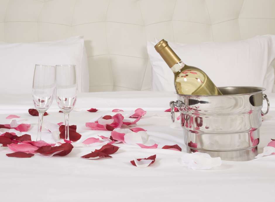 champagne and rose petals on bed